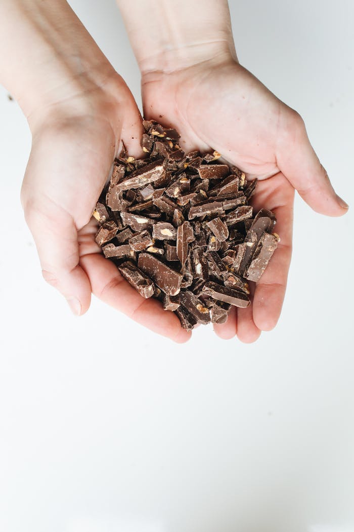 Close-up of hands cupping pieces of chopped milk chocolate on a white background.